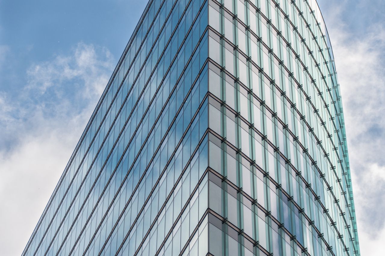 A sleek glass skyscraper reflecting the blue sky and clouds, showcasing modern architectural design.