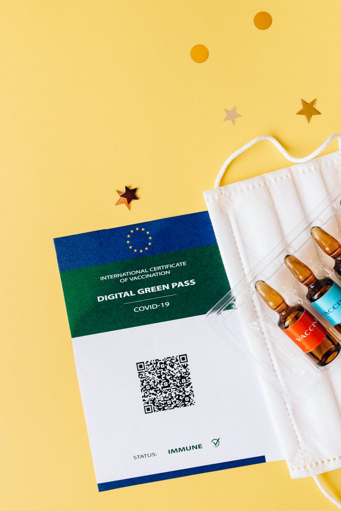 Close-up of a digital vaccination certificate with ampules and face mask on yellow background.